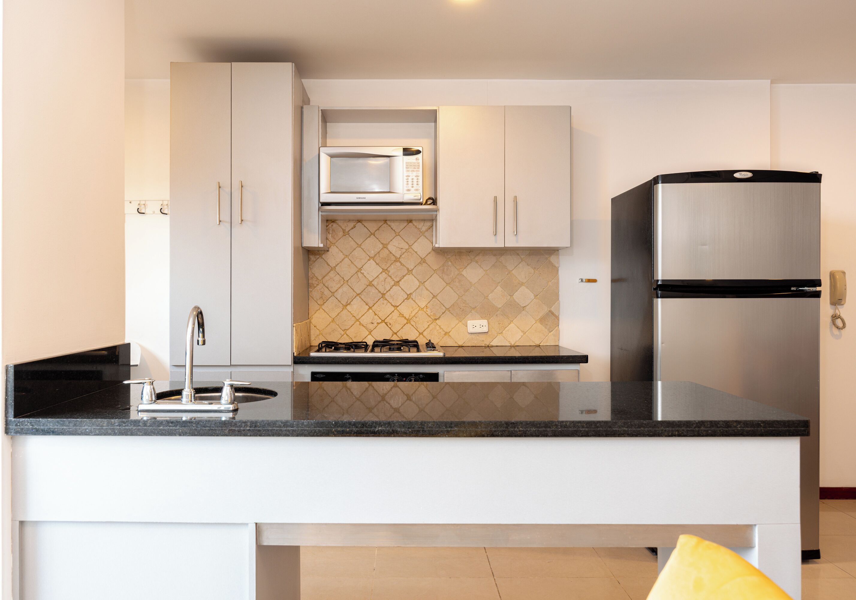 A modern kitchen with white cabinets, a black countertop, a microwave, a stove, and a refrigerator.