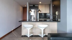 A modern kitchen with two white bar stools, a black countertop, and pendant lighting. - Apartamentos SETAI (Medellín)