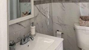 Un baño con pared de mármol, lavabo, inodoro y espejo.
