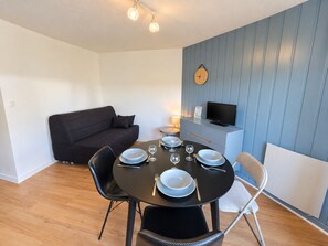 A modern living room with a dark sofa, a dining table set for four, and a television on a cabinet.