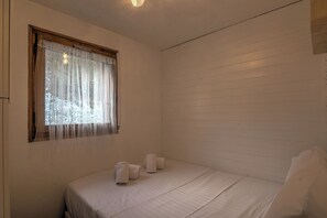 A bedroom with a single bed, a window with sheer curtains, and a wooden headboard.
