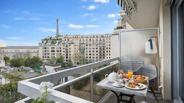 A balcony with a table set for breakfast, a wicker chair, and a view of the Eiffel Tower. - Appartement Trocadero - 4 étoiles - Welkeys (Paris)