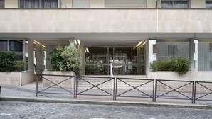 A modern building with a glass entrance, a metal fence, and potted plants. - Appartement Trocadero - 4 étoiles - Welkeys (Paris)
