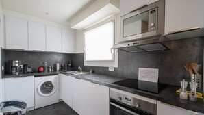 A modern kitchen with a washing machine, oven, microwave, and a note on the counter. - Appartement Trocadero - 4 étoiles - Welkeys (Paris)