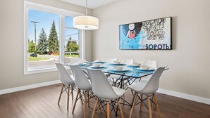 A dining area with a glass table, white chairs, and a large window with a view of trees and a road. - Spacious Central 4BR Duplex with 2 Car Garage & Downtown View from Rooftop Patio (Calgary)