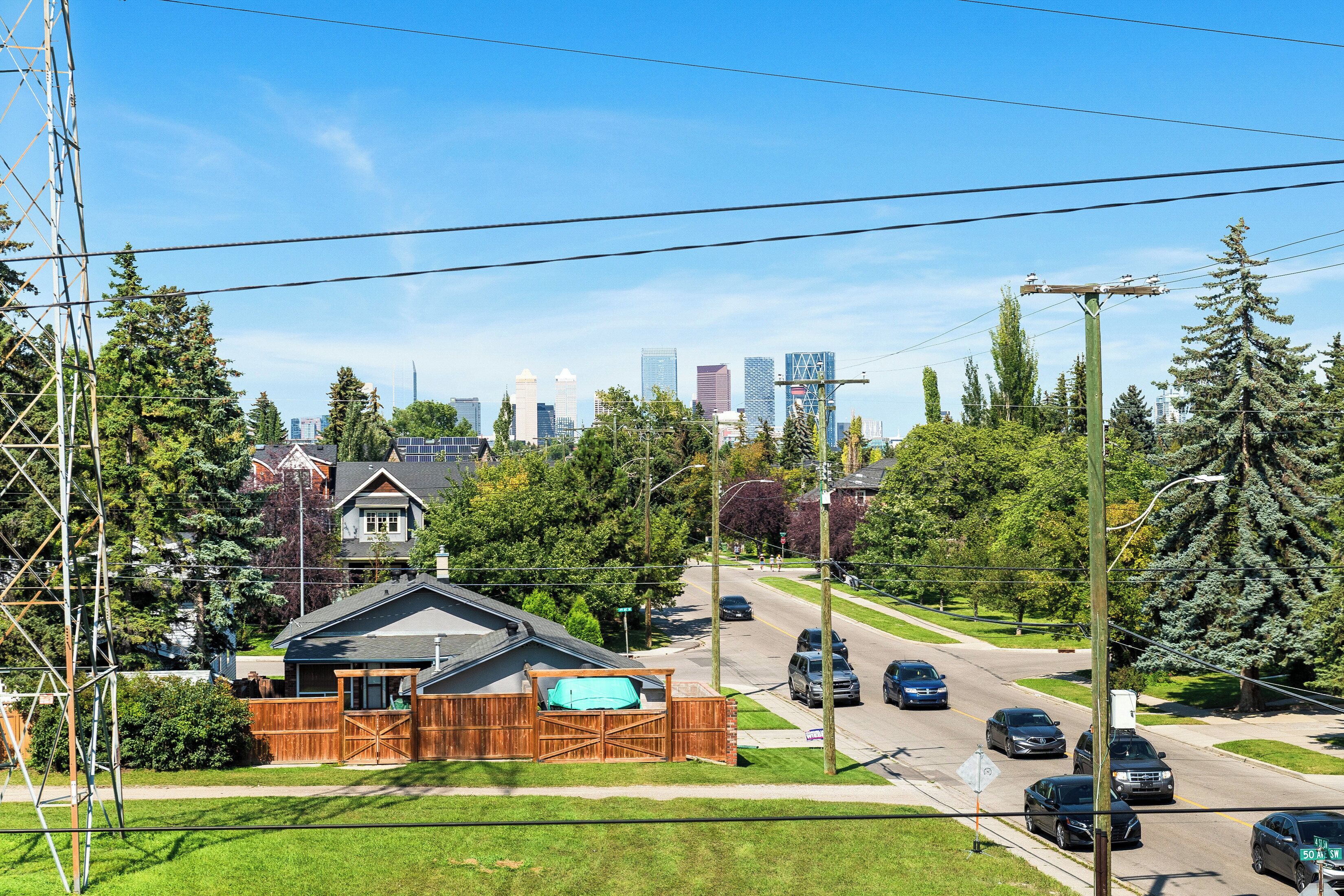 A suburban street with houses, a wooden fence, and a clear view of a city skyline in the background.
