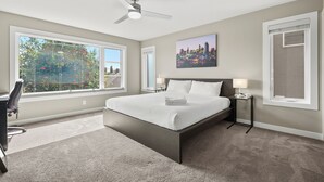 A bedroom with a large bed, a desk, a chair, a nightstand, a lamp, and a ceiling fan. - Spacious Central 4BR Duplex with 2 Car Garage & Downtown View from Rooftop Patio (Calgary)