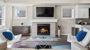 A modern living room with a fireplace, a flat-screen TV, and a glass coffee table. - Spacious Central 4BR Duplex with 2 Car Garage & Downtown View from Rooftop Patio (Calgary)