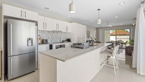 A modern kitchen with white cabinetry, a stainless steel refrigerator, and a central island with bar stools. - Spacious 4-Bed House with Secure Parking (Northgate)