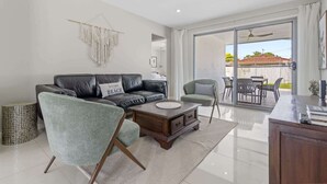A modern living room with a leather sofa, a green armchair, and a wooden coffee table. There is a sliding glass door leading to an outdoor patio area with a table and chairs. - Spacious 4-Bed House with Secure Parking (Northgate)