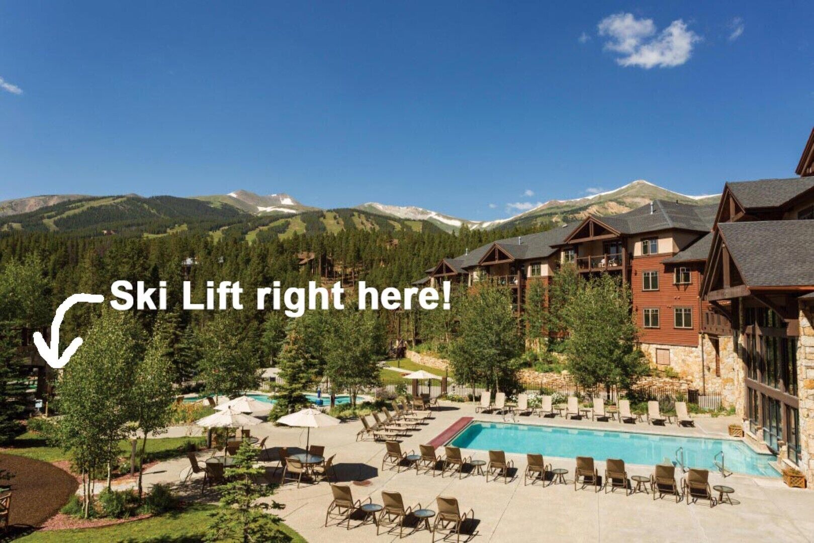 A resort with a pool, outdoor seating, and a ski lift visible in the background.