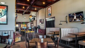 Een restaurant met houten tafels en zitbanken, een bar en een groot televisiescherm waarop een sportevenement wordt vertoond.