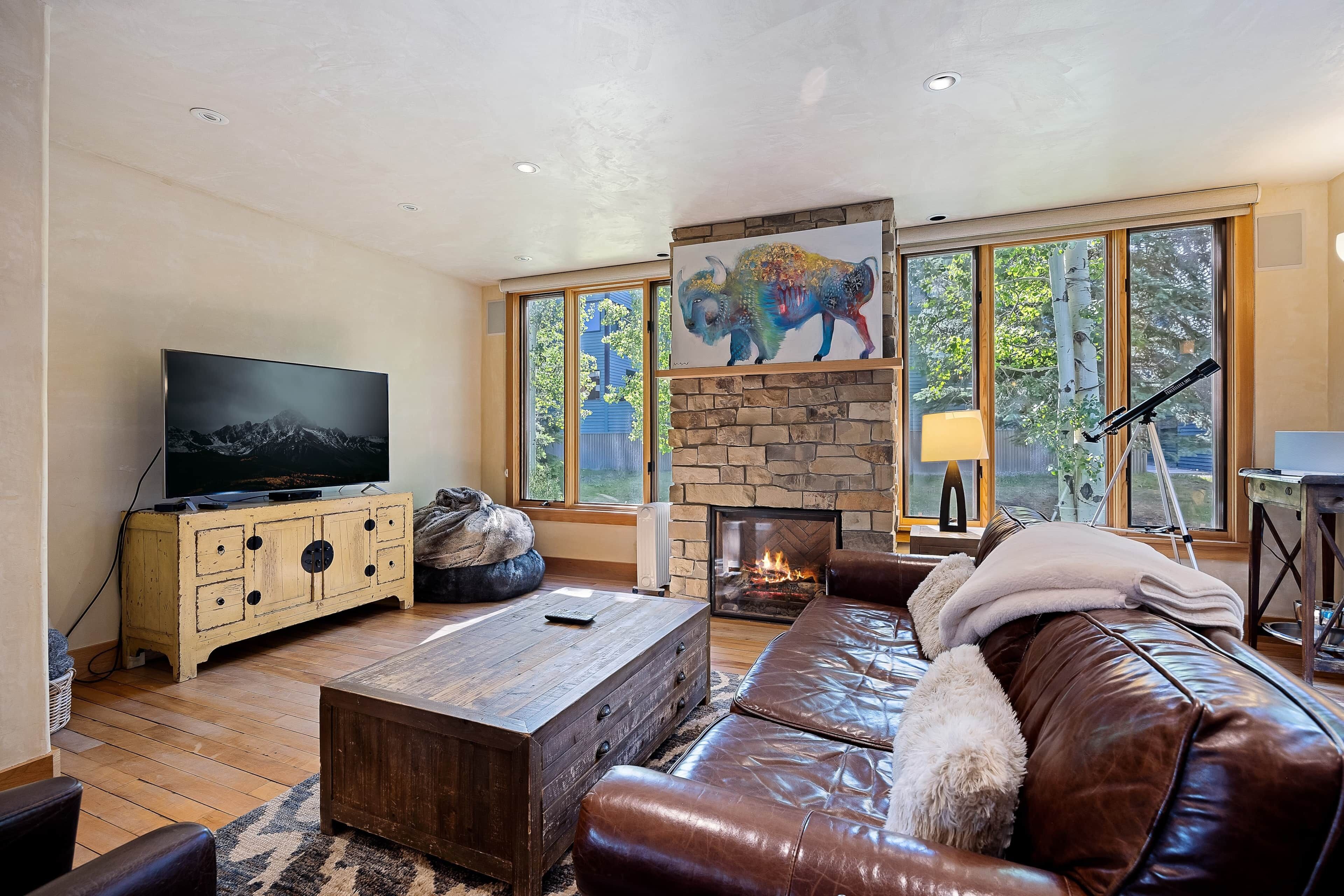 A living room with a stone fireplace, a television, and a large window with a painting.