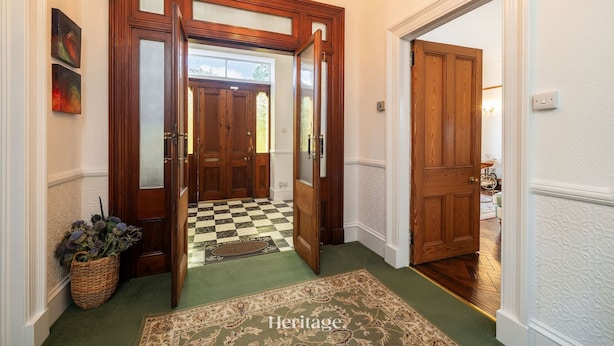 Un pasillo con puertas de madera, una alfombra a cuadros y un tapete verde que lleva a una habitación.