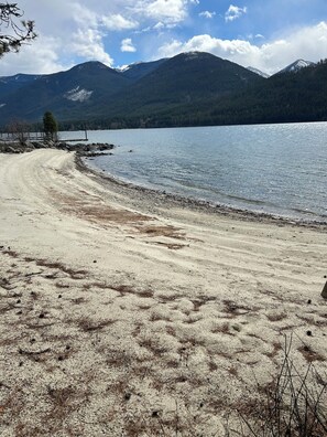 A beach with a dirt path leading to a dock, surrounded by mountains and a clear sky.