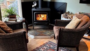Ett mysigt vardagsrum med en öppen spis, flätade fåtöljer, en mönstrad matta och en tv.