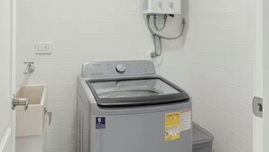 Een kleine wasruimte met een voorlader wasmachine, een wandheater en een droogrek.