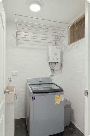 Een kleine wasruimte met een voorlader wasmachine, een wandheater en een droogrek.