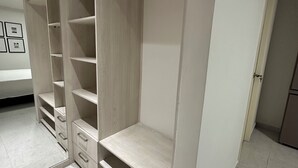 Een inloopkast met meerdere planken en lades, een spiegel en een deur naar een andere kamer.