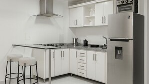 Een moderne keuken met witte kastjes, roestvrijstalen apparatuur, een gasfornuis en twee barkrukken.