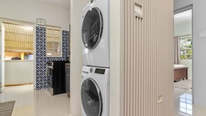 Une buanderie équipée de deux machines à laver à chargement frontal, un petit coin cuisine avec un four à micro-ondes et un évier, et une porte donnant sur une chambre.