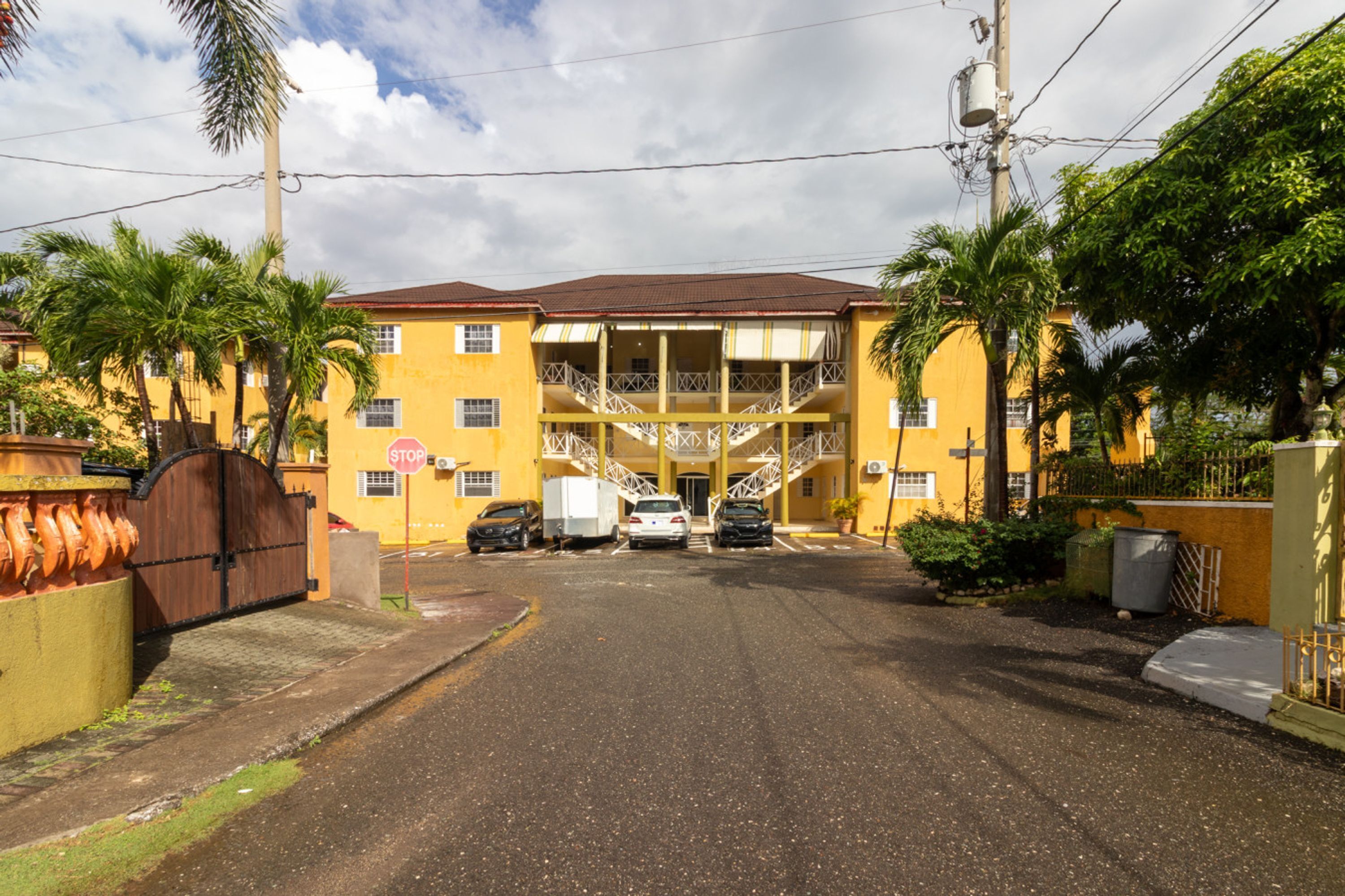 Un edificio amarillo con una escalera central, una entrada protegida por una reja y automóviles estacionados.