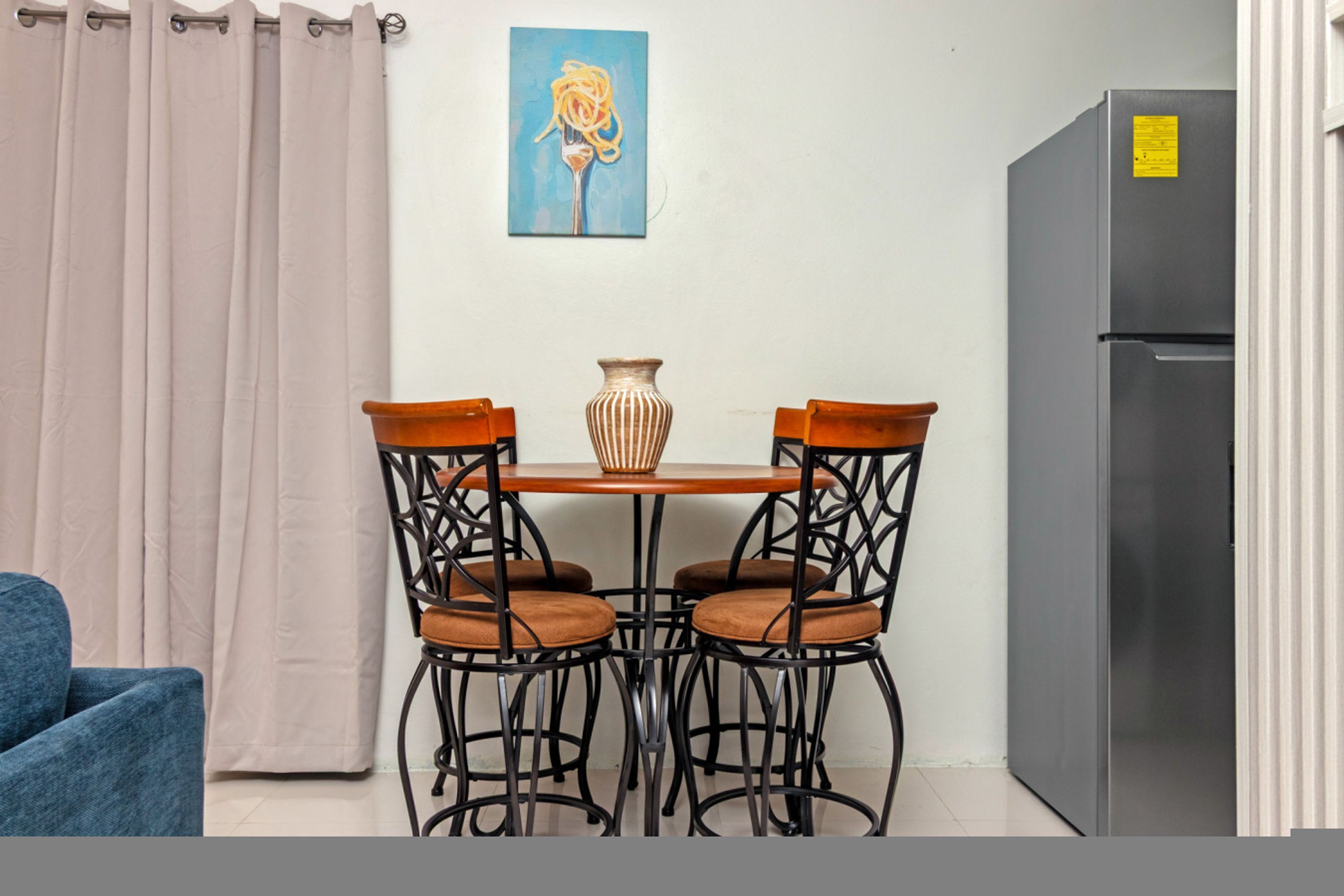 Een kleine kitchenette met een koelkast, een eettafel met vier stoelen en een vaas op de tafel.