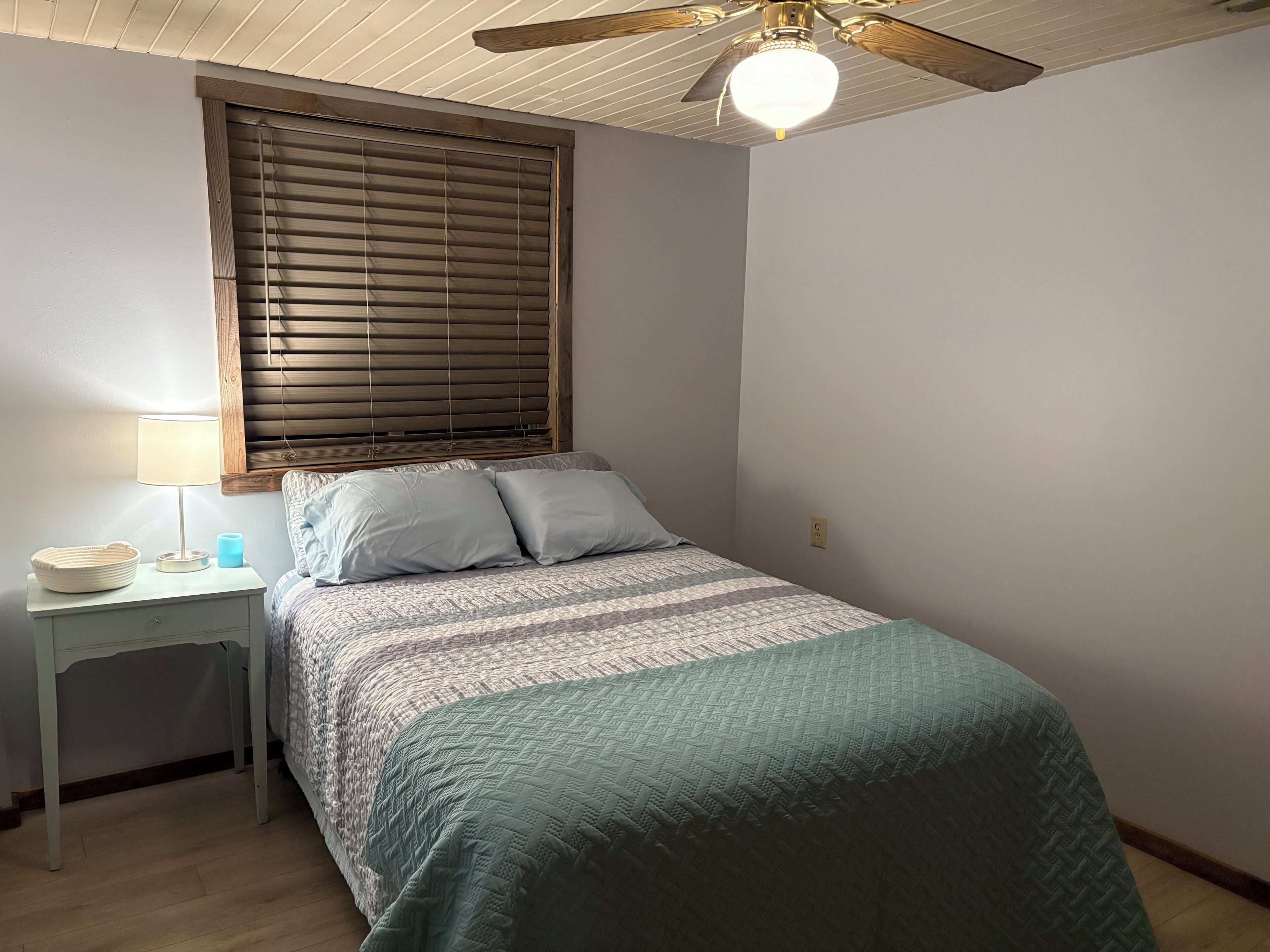 A bedroom with a bed, a nightstand, a lamp, and a ceiling fan.