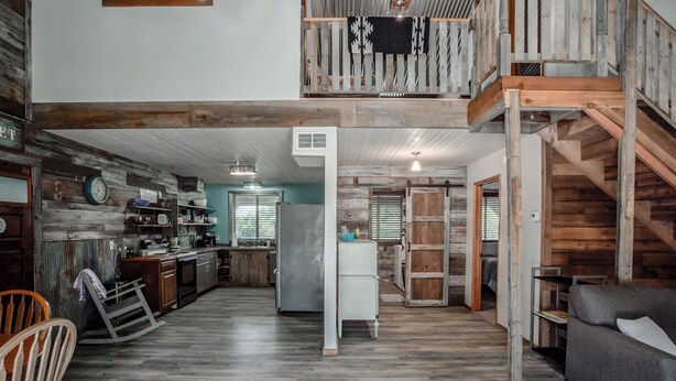 A spacious loft-style living area with a high ceiling, exposed wooden beams, and a central staircase. - Cedar Ridge Ranch Barndominium/Cozy Rustic 3-Bedroom with Wood-Burning Stove (Hutchinson)