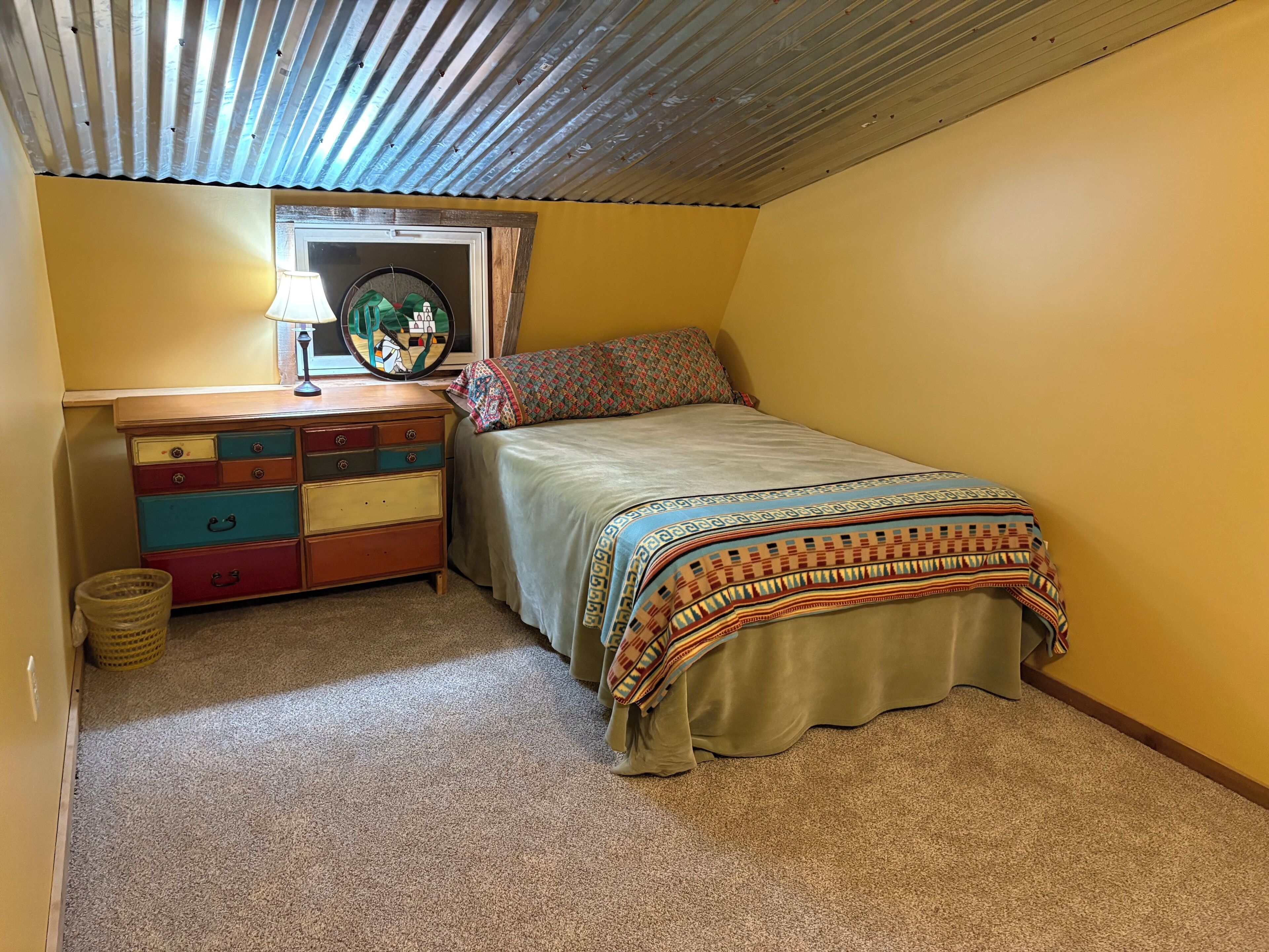 A bedroom with a bed, a dresser, a window, and a lamp.