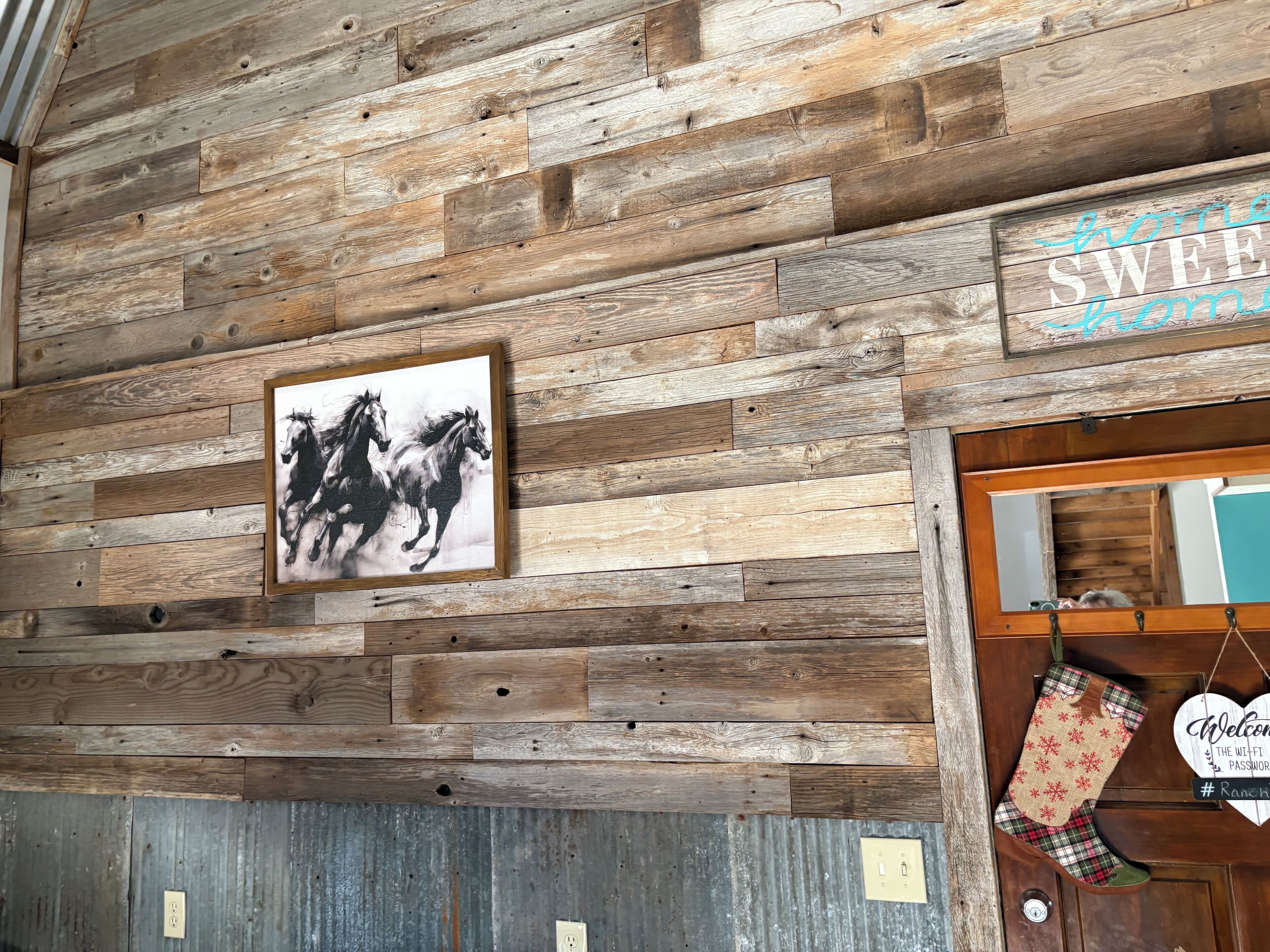 A rustic wooden wall with a framed black and white horse painting, a welcome sign, and a plaid oven mitt hanging on the door.