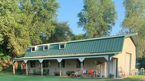 A single-story building with a green roof and a covered porch area. - Cedar Ridge Ranch Barndominium/Cozy Rustic 3-Bedroom with Wood-Burning Stove (Hutchinson)