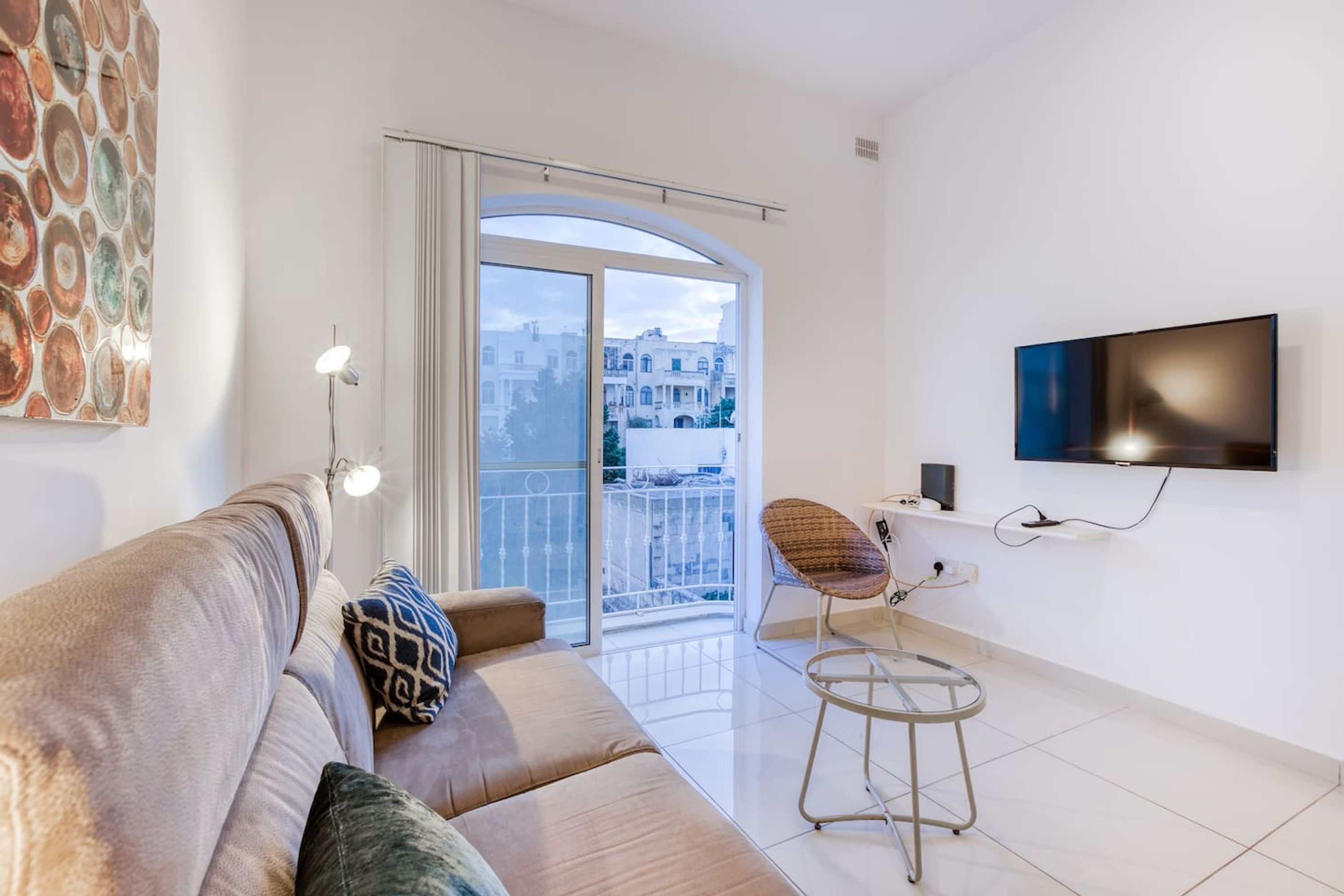 Een moderne woonkamer met een bank, een stoel, een televisie en een balkon met uitzicht over de stad.