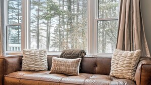 A brown leather sofa with three cushions, positioned by a window with a view of trees.