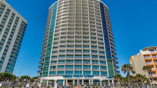 Um hotel com várias andares, fachada curva, varandas e localização à beira-mar.
