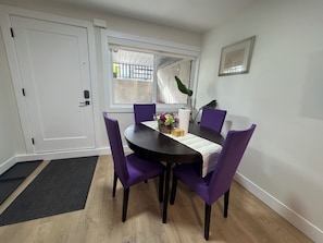Ein Essbereich mit einem runden Tisch, violetten Stühlen, einer Blumenvase und einem Fenster mit Blick.