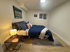Ein Schlafzimmer mit einem Bett, einem Nachttisch, einer Lampe und einem Fenster.
