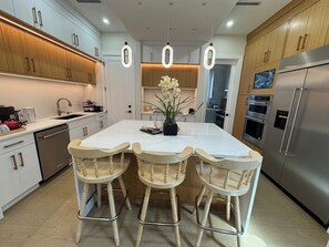 A modern kitchen with white cabinets, a stainless steel refrigerator, and a central island with bar stools. - A Luxurious Vacation Home in South Surrey (Surrey)