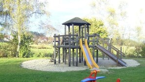 Un parque infantil con una estructura de madera, un tobogán y columpios.