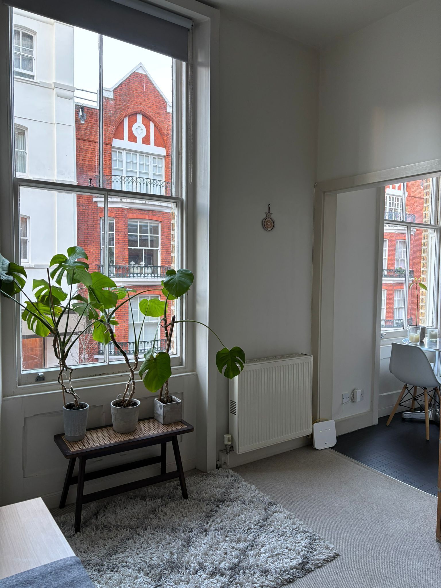 Ein Zimmer mit einem großen Fenster, einer Heizung, einer kleinen Bank und einem Stuhl.