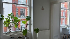 A room with a large window, a radiator, a small bench, and a chair. - Cozy flat in Marylebone (London)