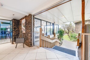 Une entrée intérieure avec un mur en pierre, un escalier en bois et une vue sur l’extérieur.