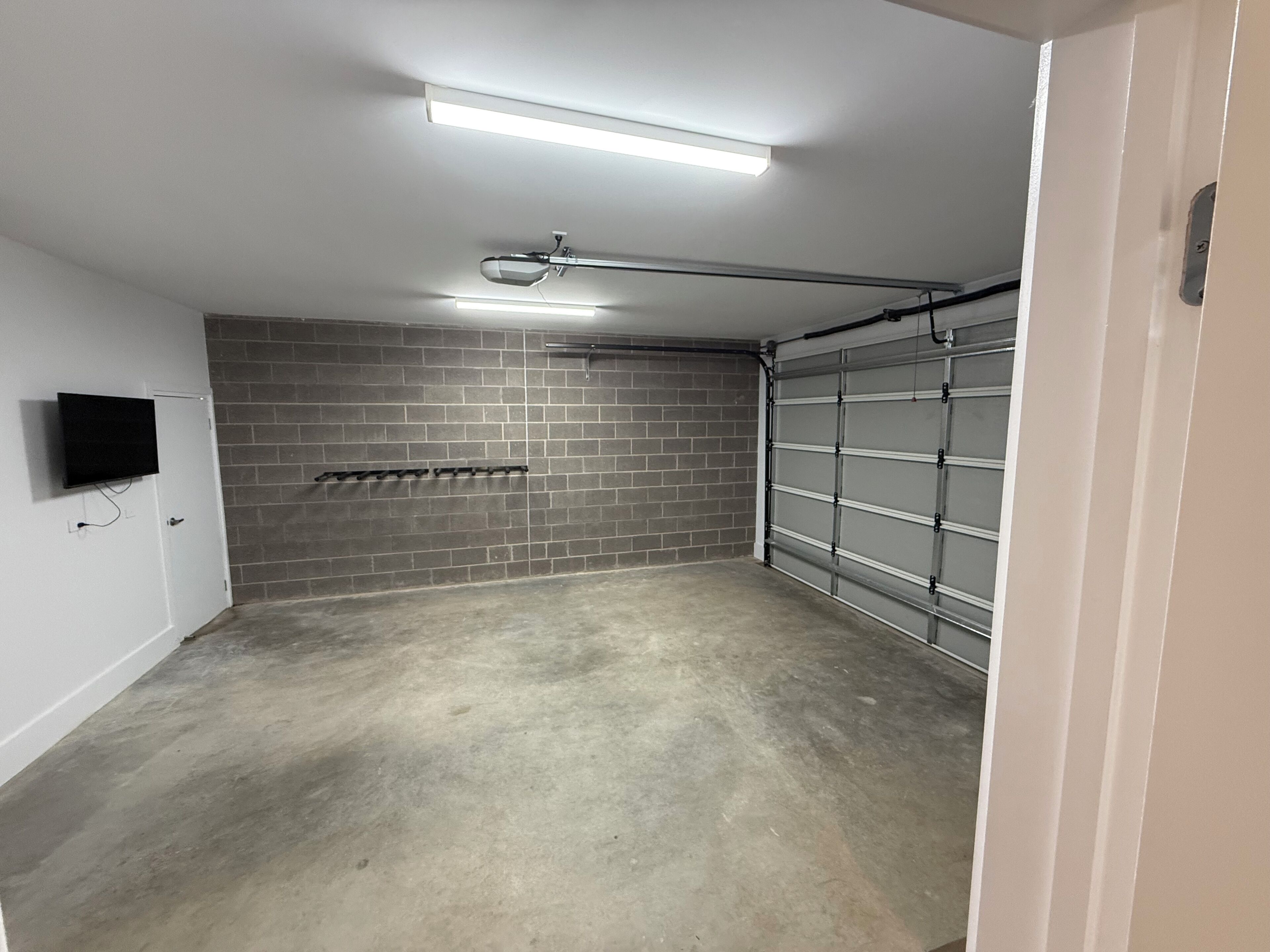 A garage with a concrete floor, a brick wall, a metal garage door, and a ceiling-mounted light fixture.