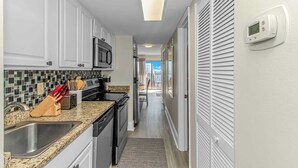 A narrow kitchen with white cabinets, a microwave, and a stove. - Ocean Villas 502 (Myrtle Beach)