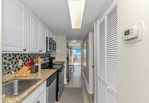 A narrow kitchen with white cabinets, a microwave, and a stove. - Ocean Villas 502 (Myrtle Beach)