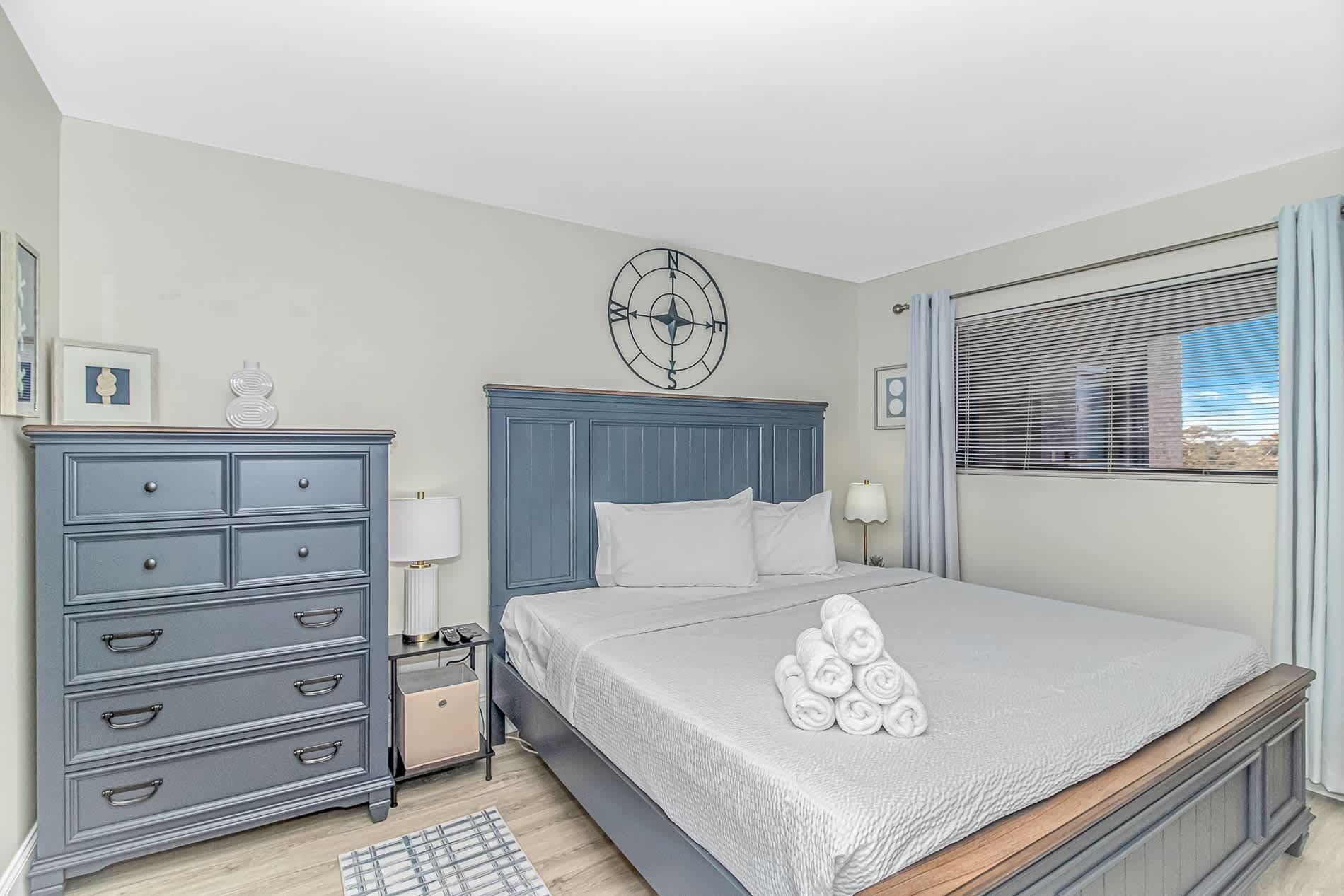 A bedroom with a bed, dresser, nightstand, lamp, and a compass wall decoration.