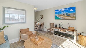 A living room with a fireplace, a dining area, and a large window with a view. - Ocean Villas 502 (Myrtle Beach)