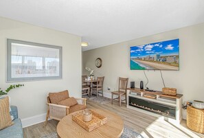 A living room with a fireplace, a dining area, and a large window with a view. - Ocean Villas 502 (Myrtle Beach)