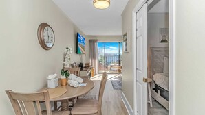 A hotel room with a balcony, a dining area with a table and chairs, and a bed with a headboard. - Ocean Villas 502 (Myrtle Beach)