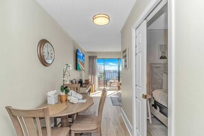 A hotel room with a balcony, a dining area with a table and chairs, and a bed with a headboard. - Ocean Villas 502 (Myrtle Beach)